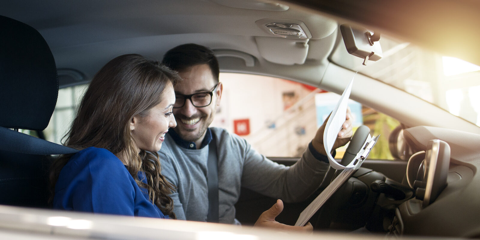 Happy couple in car interior at vehicle dealership showroom.