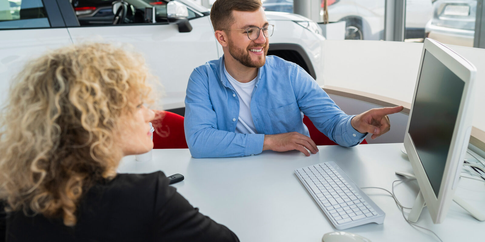 Car dealership manager with client at computer in showroom