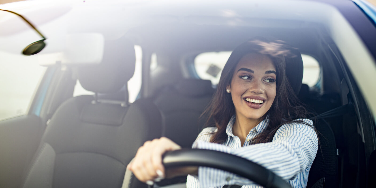 Happy woman driving a car and smiling. Cute young success happy brunette woman is driving a car. Portrait of happy female driver steering car with safety belt